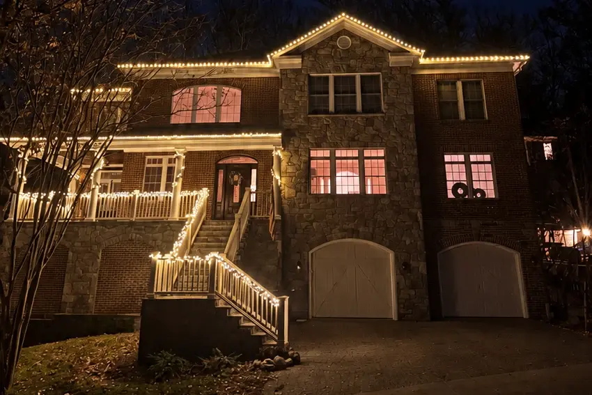The same house lit by Blink: warm white C9s on the rooflines and gable, the porch rail and both runs of the front stairs.